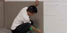 Installer applying construction adhesive to the back of a textured PS polystyrene wall panel before mounting on interior wall showing the glue-on installation method used for lightweight decorative sound absorbing wall panels Installer applying construction adhesive to the back of a textured PS polystyrene wall panel before mounting on interior wall showing the glue-on installation method used for lightweight decorative sound absorbing wall panels